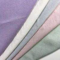 Quatre tissus pastel - lavande, blanc, rose pâle et vert pâle - sont disposés en diagonale. Le Tissu uni en viscose lyocell au mètre, lisse et respirant, de Longan Craft France, est parfait pour les peignoirs ou les chemises.