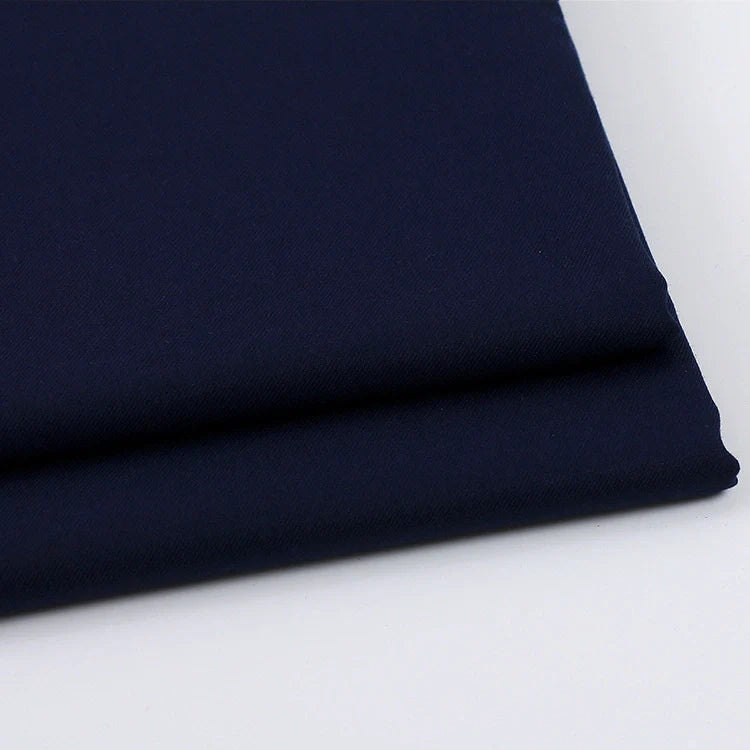 Gros plan sur deux pièces soigneusement pliées du tissu gabardine uni au mètre de Longan Craft France, un tissu mélangé de laine, de rayonne et de polyester, idéal pour une tenue décontractée, empilées sur une surface blanche.