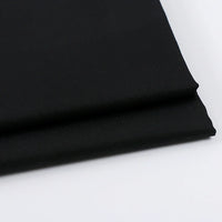 Gros plan sur deux pièces soigneusement pliées de Tissu gabardine uni au mètre de Longan Craft France, un mélange de laine, de rayonne et de polyester, idéal pour les vêtements décontractés, présenté sur une surface blanche.