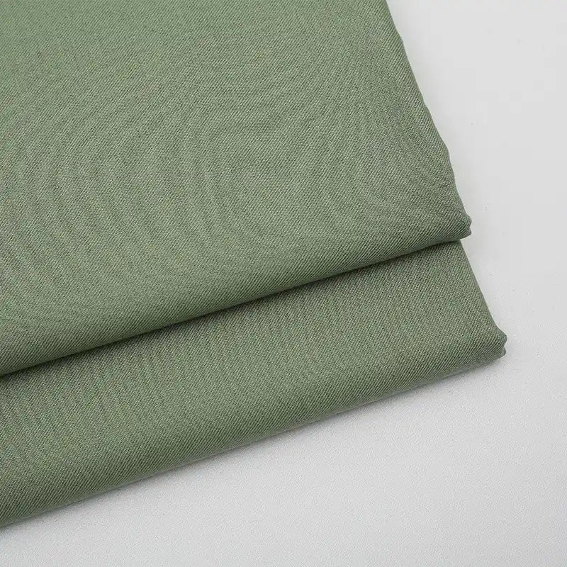 Gros plan sur deux pièces soigneusement pliées de tissu gabardine vert clair uni au mètre de Longan Craft France, un mélange de laine, de rayonne et de polyester, idéal pour les vêtements décontractés et les blazers.