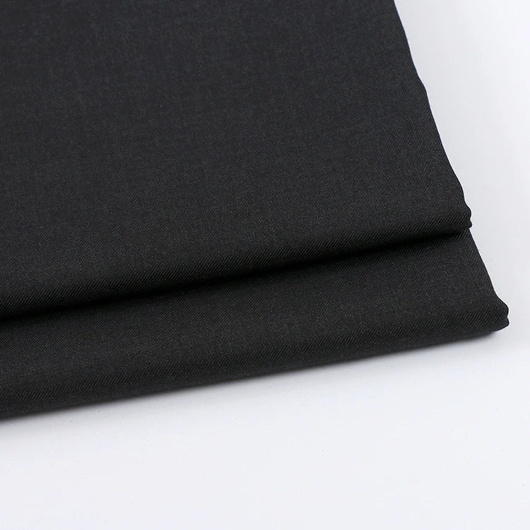 Gros plan sur deux pièces de Tissu gabardine uni au mètre de Longan Craft France, en gris foncé, sur une surface blanche - montrant sa finition lisse et légèrement texturée ; textile idéal pour les vêtements décontractés.