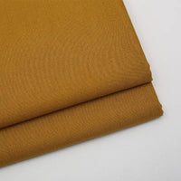 Deux pièces soigneusement pliées de Tissu gabardine uni de Longan Craft France, un mélange lisse de laine, de rayonne et de polyester de couleur jaune moutarde, sont empilées sur une surface blanche - idéal pour les vêtements décontractés.