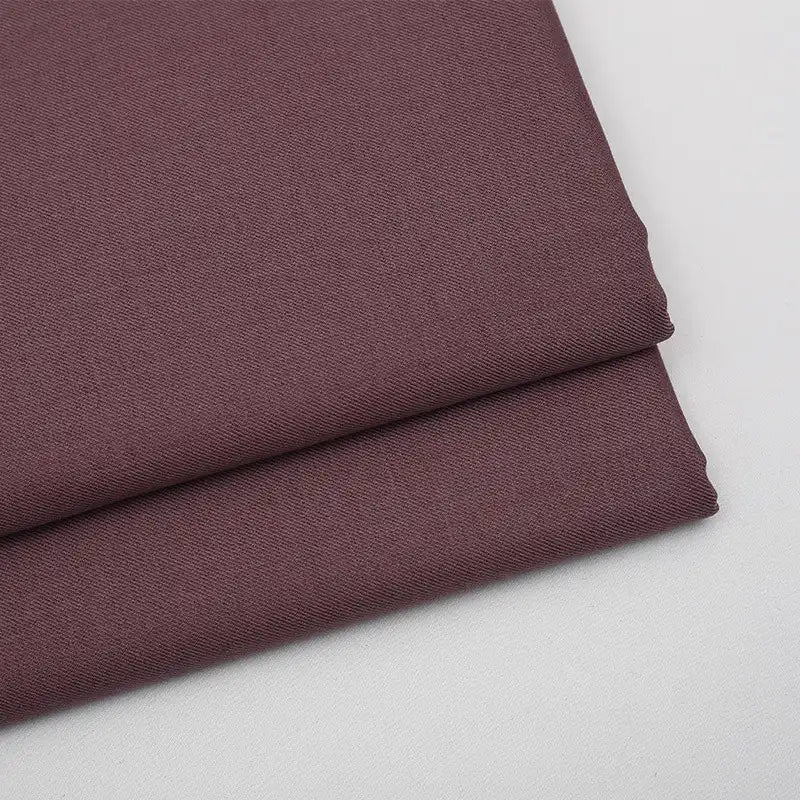 Gros plan sur deux pièces pliées de tissu gabardine marron uni de Longan Craft France, un mélange de laine, de rayonne et de polyester, idéal pour une tenue décontractée, empilées sur une surface blanche.