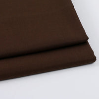 Gros plan sur deux pièces soigneusement pliées de Tissu gabardine uni au mètre de Longan Craft France, un tissu marron foncé en laine-rayon-polyester, idéal pour les vêtements décontractés, empilées sur une surface blanche.