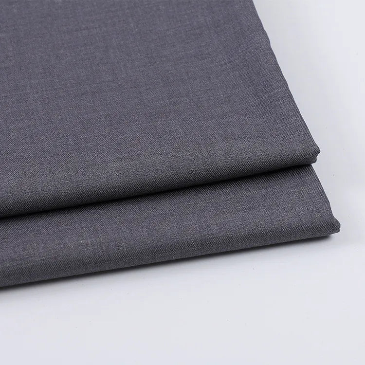 Deux pièces de Tissu gabardine uni au mètre de Longan Craft France, de couleur gris moyen, sont empilées sur une surface blanche. Lisse et tissé serré, ce mélange laine-rayon-polyester est parfait pour les vêtements décontractés et les créations sur mesure.