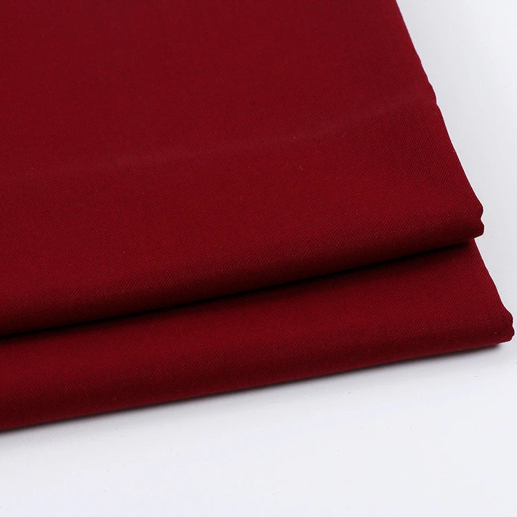 Deux pièces de Tissu gabardine uni au mètre rouge foncé plié de Longan Craft France, un mélange sergé de laine, de rayonne et de polyester, sont empilées sur une surface blanche - le textile idéal pour les vêtements décontractés.