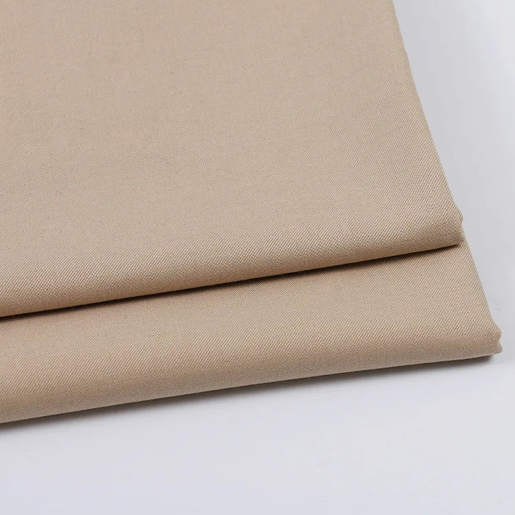 Deux pièces soigneusement pliées de Tissu gabardine uni au mètre de Longan Craft France, de couleur beige clair, sont empilées sur une surface blanche, soulignant la texture lisse et les bords nets de ce mélange laine-rayon-polyester idéal pour les tenues décontractées.