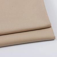 Deux pièces soigneusement pliées de Tissu gabardine uni au mètre de Longan Craft France, de couleur beige clair, sont empilées sur une surface blanche, soulignant la texture lisse et les bords nets de ce mélange laine-rayon-polyester idéal pour les tenues décontractées.