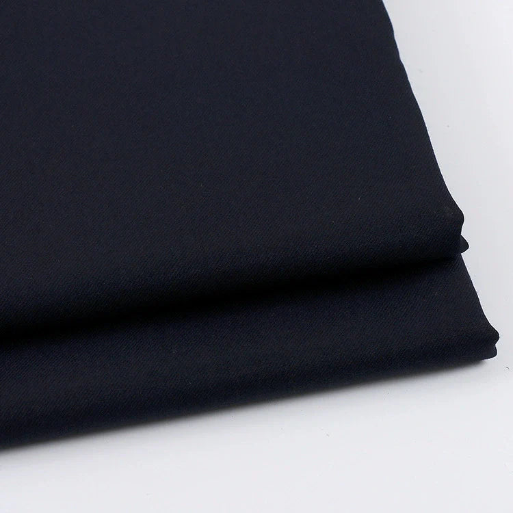 Gros plan sur deux pièces pliées du tissu gabardine uni au mètre de Longan Craft France, un tissu sergé bleu marine foncé en laine-rayonne-polyester, placé sur une surface blanche. Idéal pour les vêtements décontractés.