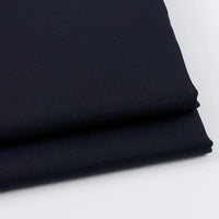 Gros plan sur deux pièces pliées du tissu gabardine uni au mètre de Longan Craft France, un tissu sergé bleu marine foncé en laine-rayonne-polyester, placé sur une surface blanche. Idéal pour les vêtements décontractés.