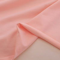 Un gros plan du Jersey coton élasthanne au mètre rose pâle de Longan Craft France, posé en douceur avec un coin plié, révèle les deux faces de ce tissu extensible parfait pour les robes de chambre.