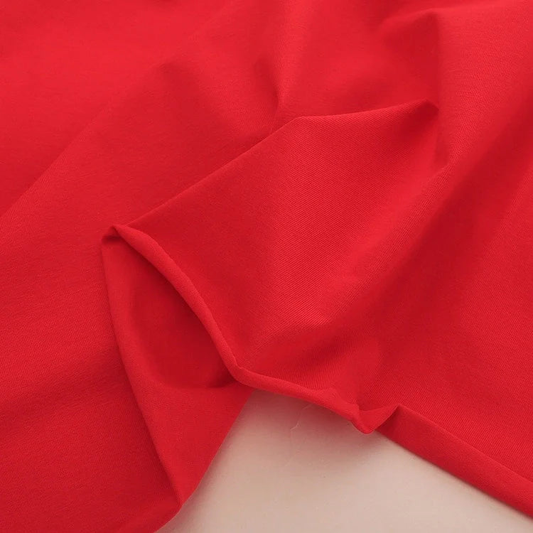 Gros plan sur le Jersey coton élasthanne au mètre rouge vif de Longan Craft France, un tissu lisse et extensible idéal pour les robes et disponible en uni tissu jersey extensible.