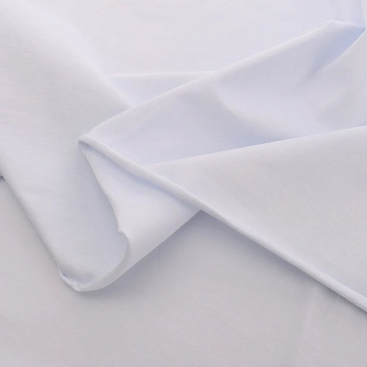 Gros plan sur le Jersey coton élasthanne au mètre de Longan Craft France, blanc et lisse, qui présente de légers plis sur un fond blanc assorti. Uni extensible en tissu jersey idéal pour les peignoirs et les projets de couture.