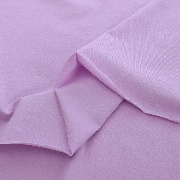 Un gros plan de Jersey coton élasthanne uni de Longan Craft France montre son tissu violet clair doux et lisse aux plis subtils - un tissu extensible aux couleurs uniformes, idéal pour les robes de chambre et les vêtements, disponible au mètre.
