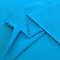 Plusieurs pièces de jersey France coton élasthanne uni en bleu vif sont superposées et pliées sur une surface plane, mettant en valeur leur texture lisse - idéal tissu extensible pour robes et vêtements.