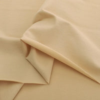 Un gros plan de Jersey coton élasthanne au mètre de Longan Craft France montre le tissu beige clair, lisse et légèrement brillant, drapé en couches souples - idéal pour la confection de robes et de vêtements extensibles.