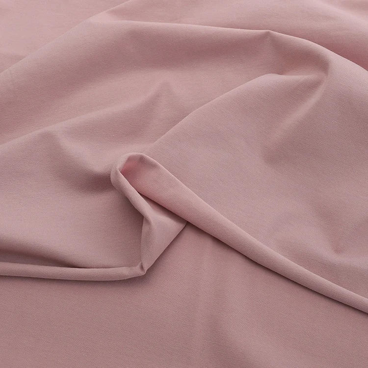 Le Jersey coton élasthanne au mètre de Longan Craft France est un tissu extensible rose clair uni, à la texture lisse et douce et aux plis subtils. Cet uni tissu jersey est idéal pour des robes et vêtements confortables sans motifs ni ornements.