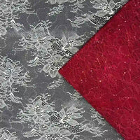 Un morceau de tissu dentelle pailleté avec sequins au mètre de Longan Craft France est posé en diagonale sur une dentelle rouge, toutes deux ornées de motifs floraux. La dentelle blanche à paillettes est transparente, tandis que le tissu rouge pour robes est opaque et texturé.