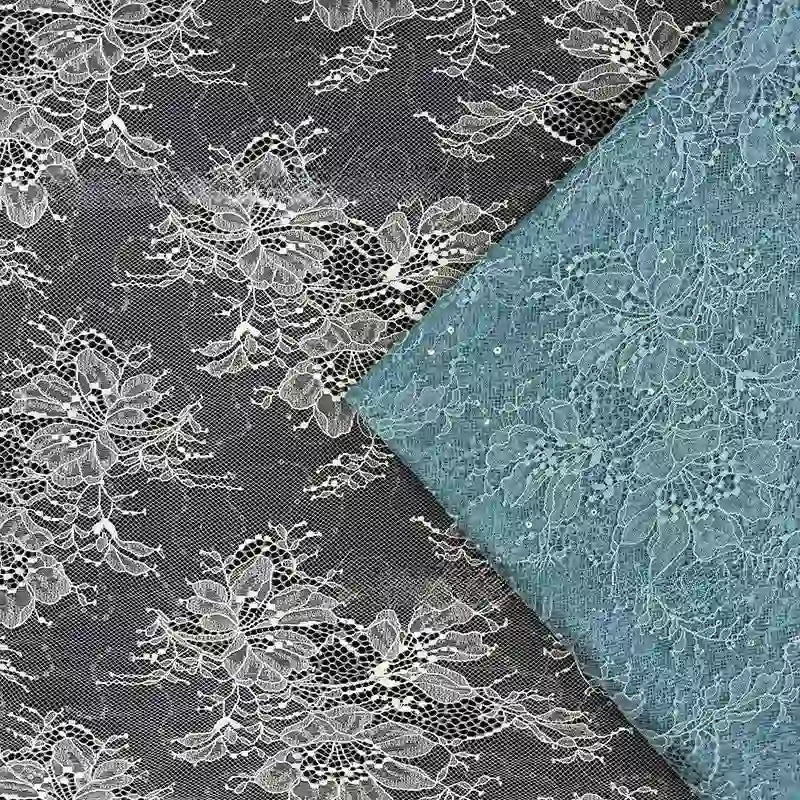Une bande de Tissu dentelle pailleté avec paillettes au mètre de Longan Craft France repose en diagonale sur une plus grande dentelle noire à motifs floraux blancs, mettant en valeur le contraste saisissant et l'élégance de ces tissus prêts à être utilisés en robe de chambre.