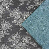 Une bande de Tissu dentelle pailleté avec paillettes au mètre de Longan Craft France repose en diagonale sur une plus grande dentelle noire à motifs floraux blancs, mettant en valeur le contraste saisissant et l'élégance de ces tissus prêts à être utilisés en robe de chambre.