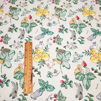 Une règle en bois repose sur le Tissu motif Pâques lapin de printemps au mètre de Longan Craft France, qui présente des lapins, des fleurs, des feuilles et des fraises illustrés sur un tissu de coton léger - idéal pour les créations et décorations printanières.