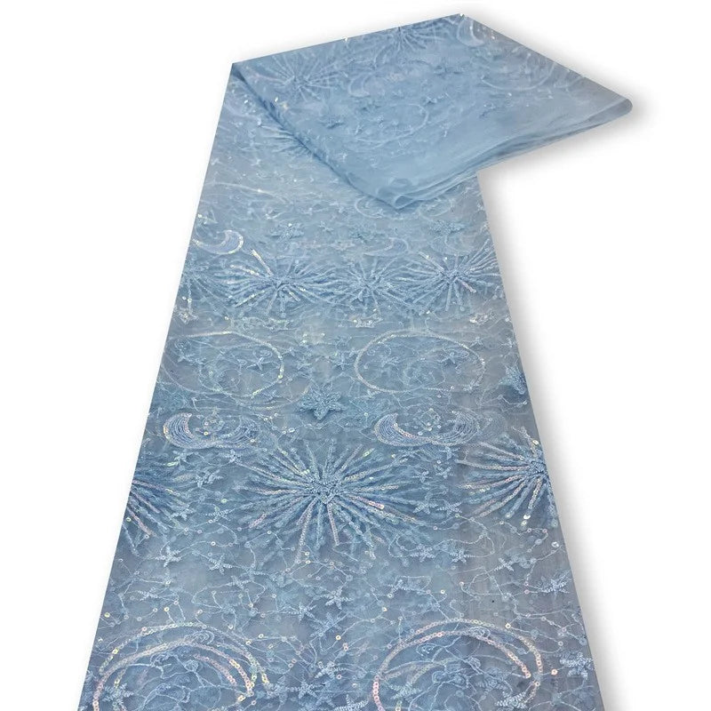 Un morceau plié de tissu bleu clair "Tulle brodé de sequins étoiles et lunes" de Longan Craft France, présentant des motifs de paillettes étoiles et lunes, est présenté sur un fond blanc - parfait pour confectionner des robes étincelantes.