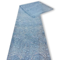 Un morceau plié de tissu bleu clair "Tulle brodé de sequins étoiles et lunes" de Longan Craft France, présentant des motifs de paillettes étoiles et lunes, est présenté sur un fond blanc - parfait pour confectionner des robes étincelantes.
