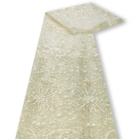 Le tulle brodé de sequins étoiles et lunes au mètre de Longan Craft France est un tissu transparent beige clair brodé de sequins blancs et argentés, parfait pour les robes. Présenté sur un fond blanc.