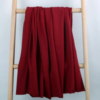 Le Longan Craft France Tissu French Terry en coton extensible au mètre, un tissu tricoté multicolore confortable idéal pour vêtements de sport, est présenté drapé sur une échelle en bois clair devant un fond bleu clair.