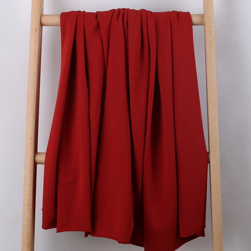 Un morceau de Longan Craft France Tissu French Terry en coton extensible au mètre, une maille multicolore confortable idéale pour les vêtements de sport, est drapé sur une échelle en bois clair sur un fond blanc uni.