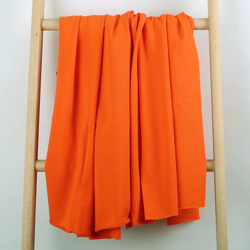 Un tissu multicolore en coton extensible French Terry de Longan Craft France est drapé sur une échelle en bois clair, présentée sur un fond blanc uni.