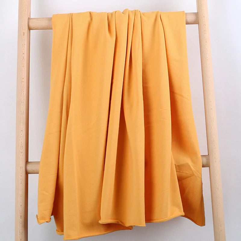 Le "Tissu French Terry en coton extensible au mètre" de Longan Craft France, un tissu tricoté multicolore et confortable pour vêtements de sport, est drapé sur une échelle en bois clair devant un fond blanc uni.