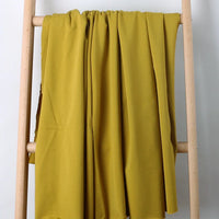 Un Tissu French Terry en coton extensible jaune moutarde de Longan Craft France est drapé sur une échelle en bois clair, sur un fond blanc uni.