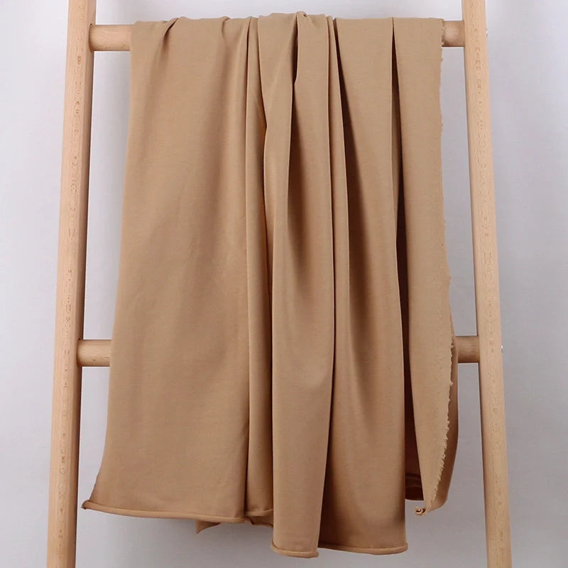 Une longueur de Tissu French Terry en coton extensible au mètre de Longan Craft France est drapée sur une échelle en bois clair sur un fond blanc uni.