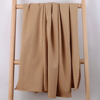 Une longueur de Tissu French Terry en coton extensible au mètre de Longan Craft France est drapée sur une échelle en bois clair sur un fond blanc uni.