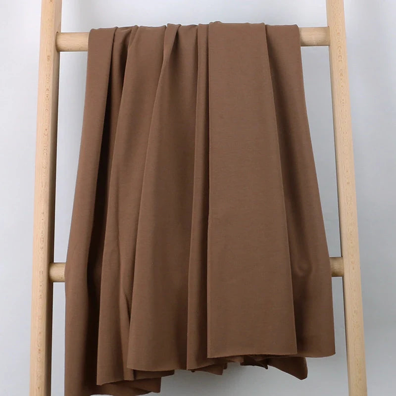 Un grand morceau de Longan Craft France Tissu French Terry en coton extensible au mètre, idéal pour vêtements de sport, est drapé sur les barreaux d'une échelle en bois clair devant un fond neutre.