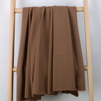 Un grand morceau de Longan Craft France Tissu French Terry en coton extensible au mètre, idéal pour vêtements de sport, est drapé sur les barreaux d'une échelle en bois clair devant un fond neutre.