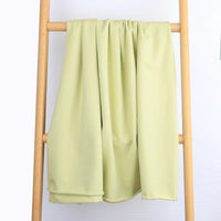 Un tissu multicolore en coton extensible French Terry de Longan Craft France est drapé sur le barreau central d'une échelle en bois clair sur un fond blanc uni. Ce tissu est parfait pour les vêtements de sport et est vendu au mètre.