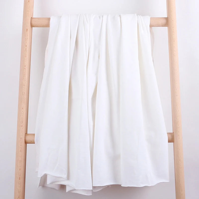 Un morceau de Tissu French Terry en coton extensible de Longan Craft France est drapé sur les barreaux centraux d'une échelle en bois clair, sur un fond blanc uni. Ce tissu confortable et multicolore est idéal pour les vêtements de sport.