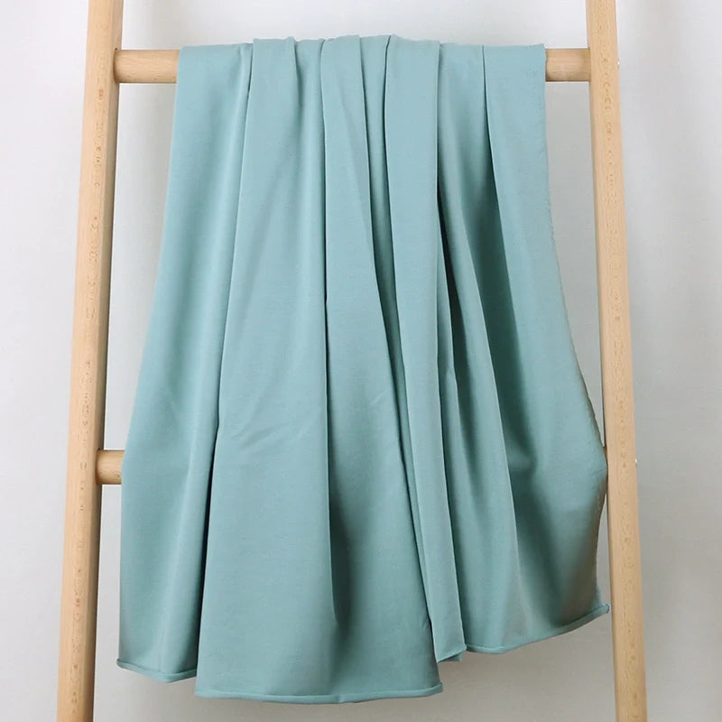 Le Tissu French Terry en coton extensible au mètre de Longan Craft France, tricoté multicolore et confortable, est drapé sur une échelle en bois clair devant un fond blanc, tombant en plis doux et élégants. Idéal pour vêtements de sport.