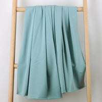 Le Tissu French Terry en coton extensible au mètre de Longan Craft France, tricoté multicolore et confortable, est drapé sur une échelle en bois clair devant un fond blanc, tombant en plis doux et élégants. Idéal pour vêtements de sport.