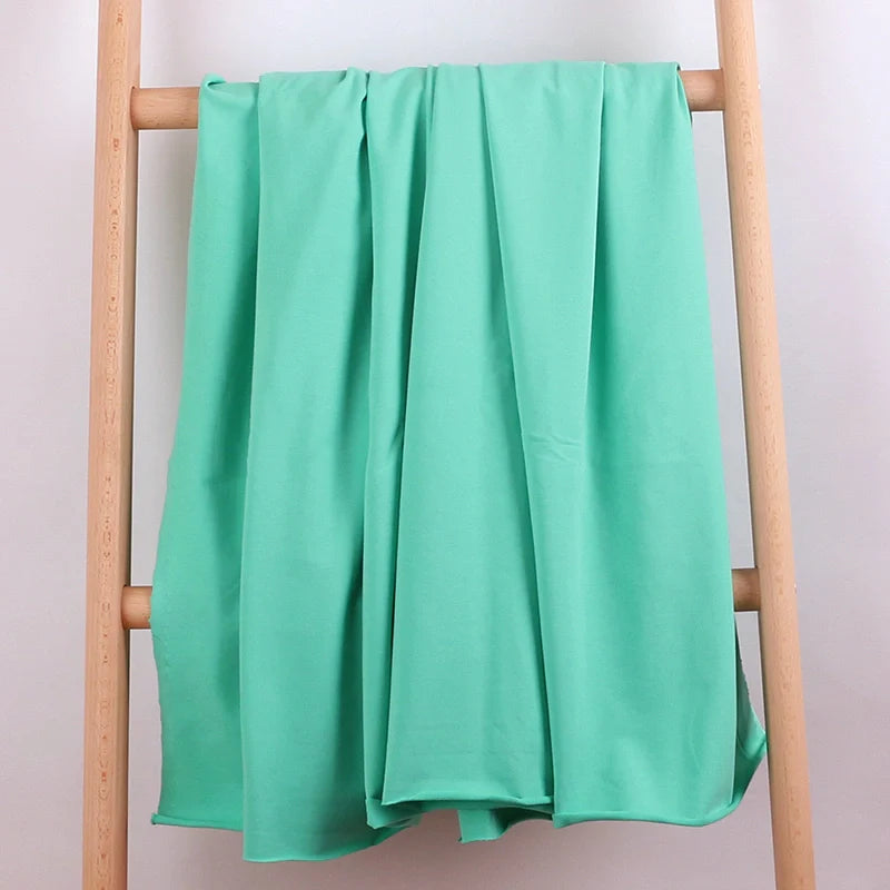 Une échelle en bois léger présente le tissu de coton multicolore French Terry de Longan Craft France, idéal pour les vêtements de sport, drapé sur ses barreaux sur un fond blanc uni.