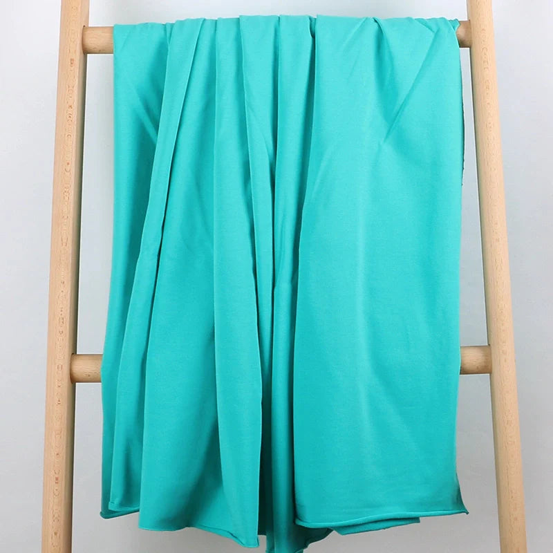 Un tissu multicolore en coton stretch French Terry de Longan Craft France est présenté drapé sur une échelle en bois clair sur fond blanc, idéal pour des vêtements de sport confortables et vendu au mètre.