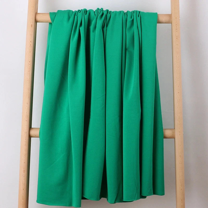 Un morceau de Longan Craft France Tissu French Terry en coton extensible multicolore est drapé sur une échelle en bois léger sur un fond blanc uni - le tissu idéal pour des vêtements de sport confortables.