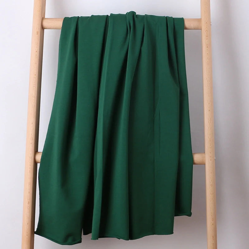 Une longueur de tissu French Terry multicolore en coton extensible de Longan Craft France est drapée sur une échelle en bois clair sur un fond blanc uni, montrant sa texture confortable, idéale pour les vêtements de sport.