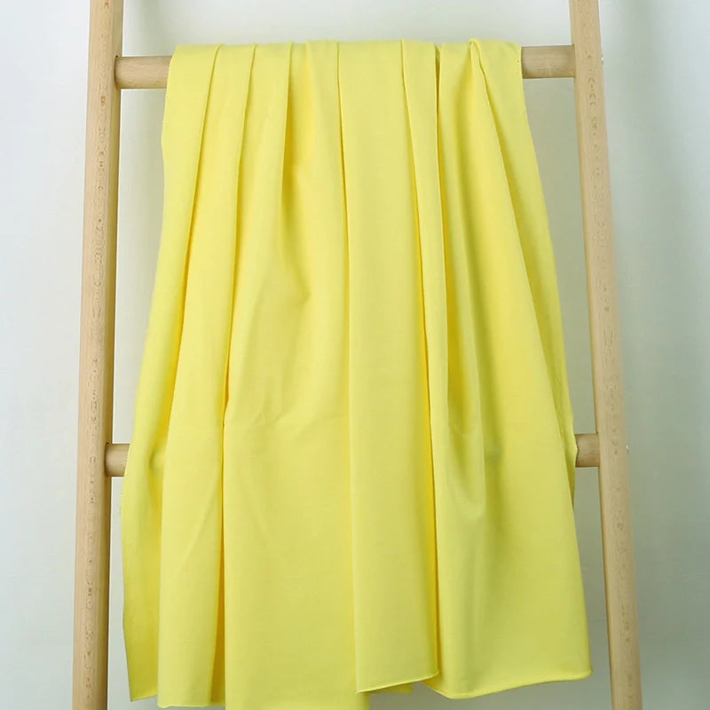Un morceau de Tissu French Terry en coton extensible de Longan Craft France, dans une teinte jaune clair, est drapé sur une échelle en bois à deux échelons sur un fond blanc uni - parfait pour créer des vêtements de sport confortables.