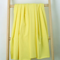 Un morceau de Tissu French Terry en coton extensible de Longan Craft France, dans une teinte jaune clair, est drapé sur une échelle en bois à deux échelons sur un fond blanc uni - parfait pour créer des vêtements de sport confortables.