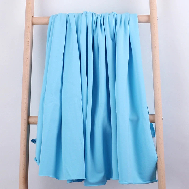 Un coton éponge extensible de Longan Craft France est drapé sur une échelle en bois léger, présentée sur un fond uni. Ce tissu au mètre, idéal pour les vêtements de sport, est suspendu en plis lâches.