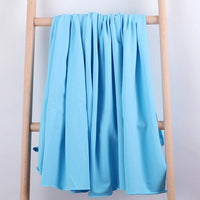 Un coton éponge extensible de Longan Craft France est drapé sur une échelle en bois léger, présentée sur un fond uni. Ce tissu au mètre, idéal pour les vêtements de sport, est suspendu en plis lâches.