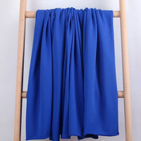 Le Tissu French Terry en coton extensible au mètre de Longan Craft France, d'un bleu royal éclatant, est drapé sur une échelle en bois clair, sur un fond blanc uni.